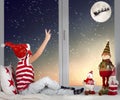 Merry Christmas .boy sitting on the window and looking at Santa Claus flying in his sleigh against moon sky. Royalty Free Stock Photo