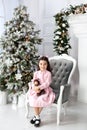 Merry Christmas and happy holidays! New Year 2020. Happy little girl in dress plays with teddy bear on an armchair in living room. Royalty Free Stock Photo