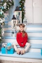 Merry Christmas, happy holidays! New Year. little girl in sweater with gift sits on porch of house. child sits on veranda decorate