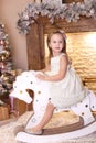 Merry Christmas, happy holidays! New Year 2020. Little girl in a white dress rides a wooden horse at home. A child riding a cardb