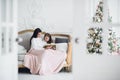 Merry Christmas and Happy Holidays. Pretty young mom reading a book to her cute daughter near Christmas tree indoors Royalty Free Stock Photo