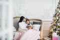 Merry Christmas and Happy Holidays. Pretty young mom reading a book to her cute daughter near Christmas tree indoors Royalty Free Stock Photo