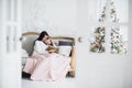 Merry Christmas and Happy Holidays. Pretty young mom reading a book to her cute daughter near Christmas tree indoors Royalty Free Stock Photo