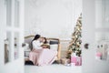 Merry Christmas and Happy Holidays. Pretty young mom reading a book to her cute daughter near Christmas tree indoors Royalty Free Stock Photo