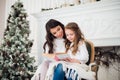 Merry Christmas and Happy Holidays, Pretty young mom reading a book to her cute daughter near tree indoors. Royalty Free Stock Photo