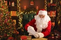 Santa Clause is prepares gifts for children for Xmas at his desk while reading wish lists Royalty Free Stock Photo