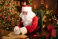 Santa Clause is prepares gifts for children for Xmas at his desk at home while opening wish lists Royalty Free Stock Photo
