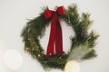 Merry Christmas and Happy Holidays! Stylish christmas wreath with red bow and golden lights hanging on white wall. Simple Royalty Free Stock Photo