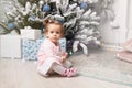 Beautiful cute little girl sitting on the floor near the New Year tree. Holiday mood, childlike spontaneity and sweet atmosphere Royalty Free Stock Photo