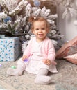 Beautiful cute little girl sitting on the floor near the New Year tree. Holiday mood, childlike spontaneity and sweet atmosphere Royalty Free Stock Photo