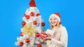 Merry Christmas and Happy New Year. Blonde girl near decorated Christmas tree opening gift box. Smiling woman in Santa Royalty Free Stock Photo