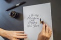 Merry christmas and a happy new year. Calligrapher Young Woman writes phrase on white paper. Inscribing ornamental Royalty Free Stock Photo