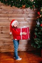 Merry Christmas and Happy New year. Cute little child girl with big red present gift box near tree indoor Royalty Free Stock Photo