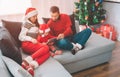 Merry Christmas and Happy New Year. Family in warm clothes and hats sitting together on sofa. They watch. Girl holds