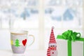 Merry Christmas and Happy New Year greeting card. A snowman, a gift package and a Christmas cup on the table in front of abstract Royalty Free Stock Photo