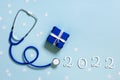 Merry Christmas and Happy New Year medicine concept, blue stethoscope, snowflakes, small gift box present, text 2022