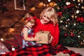 Merry Christmas and Happy New Year! Mother gives gift box to a child in living room decorated by christmas tree and xmas gift