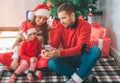 Merry Christmas and Happy New Year. Nice family sits together at Christmas tree. Man holds phone in hands and shows it