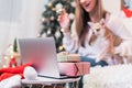 Merry Christmas and happy new year. Woman and puppy dog in sweater having a video call chat on laptop, enjoy winter