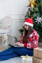 Young woman sitting near Christmas tree in a decorated living room working on laptop computer Royalty Free Stock Photo