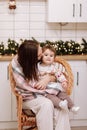 Merry Christmas and Happy New Years Holidays. Young mother hugging and kissing her baby daughter, sitting and relaxing Royalty Free Stock Photo