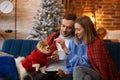 Merry Christmas. Happy young couple playing with Pomeranian Spitz dog sitting near beautiful Christmas tree at home Royalty Free Stock Photo