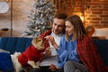 Merry Christmas. Happy young couple playing with Pomeranian Spitz dog sitting near beautiful Christmas tree at home Royalty Free Stock Photo