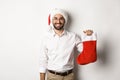 Merry christmas, holidays concept. Happy adult man receive gifts in xmas sock, looking excited, wearing santa hat, white