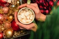 Merry Christmas home warmth post card. Hands holding cup of hot cocoa drink with marshmallow over Xmas decoration box