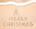 Merry Christmas inscription on wet yellow beach sand Royalty Free Stock Photo