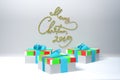 Merry Christmas 2019 lettering written by green and red spripe on white wall and three colorful present gift boxes with Royalty Free Stock Photo