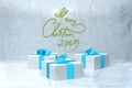 Merry Christmas 2019 lettering written by red and green striped ribbon on ice snowy wall and three present gift boxes Royalty Free Stock Photo