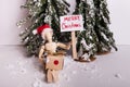 Merry Christmas picket sign held by wooden jointed wearing Santa hat holding a present on winter scene