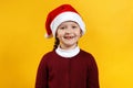 Merry Christmas. Portrait of a cheerful funny baby in Santas hat. Little girl close-up on a yellow background