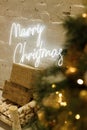 Merry Christmas sign positioned alongside a Christmas tree, adorned with lights and decorations. Royalty Free Stock Photo