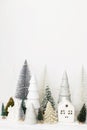 Merry Christmas! Stylish little Christmas trees and house decorations on white table. Modern christmas scene, miniature snowy