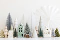 Merry Christmas! Stylish little Christmas trees and house decorations on white table. Modern christmas scene, miniature snowy