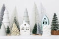 Merry Christmas! Stylish little Christmas trees and house decorations on white table. Modern christmas scene, miniature snowy