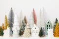 Merry Christmas! Stylish little Christmas trees and houses decorations on white table. Modern christmas scene, miniature cozy Royalty Free Stock Photo