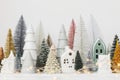 Merry Christmas! Stylish little Christmas trees and houses decorations on white table. Modern christmas scene, miniature cozy Royalty Free Stock Photo