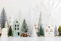 Merry Christmas! Stylish little Christmas trees and houses decorations on white table. Modern christmas scene, miniature cozy Royalty Free Stock Photo