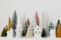 Merry Christmas! Stylish little Christmas trees and houses decorations on white table. Modern christmas scene, miniature cozy Royalty Free Stock Photo