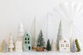 Merry Christmas! Stylish little Christmas trees and houses decorations on white table. Modern christmas scene, miniature cozy Royalty Free Stock Photo