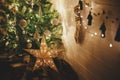 Merry Christmas! Stylish Christmas star, tree with white baubles, boho ornaments, golden lights and gifts in atmospheric evening