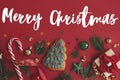 Merry Christmas text on christmas tree cookie, gift, baubles, fir branches, confetti on red background flat lay. Season`s greetin