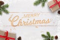 Merry Christmas text hand carved in white woodej surface surrounded with Christmas gifts, fir branches and pinecones Royalty Free Stock Photo