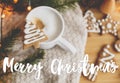 Merry Christmas text handwritten on tree gingerbread cookie on coffee at cozy knitted sweater, pine cones, fir branches and