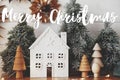 Merry Christmas text on christmas little house, trees, golden lights. Magic winter village. Season`s greetings card. Handwritten Royalty Free Stock Photo