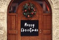 Merry Christmas text sign on  empty board with copy space on rustic wooden doors and stylish christmas wreath with red and green Royalty Free Stock Photo