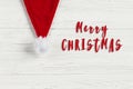 merry christmas text sign on red santa hat on white rustic wooden background. space for text. holiday greeting card concept. Royalty Free Stock Photo